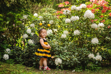 one year old child dressed up like a bee on blooming bush background