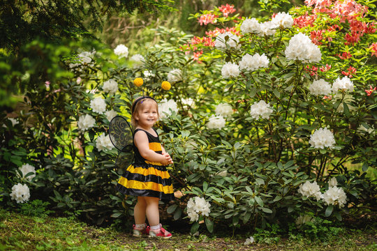 one year old child dressed up like a bee on blooming bush background