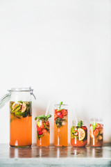 Homemade strawberry and basil lemonade or ice tea in glass and tumblers with eco-friendly plastic-free straws on grey concrete table, white wall at background, copy space. Cold refreshing soft drink