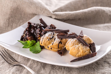 Homemade profiteroles dessert with chocolate and mint leaf on white plate on grey tablecloth