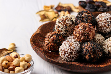 Healthy energy balls of nuts, oatmeals and dried fruit with coconut, flax and sesame seeds on coconut wooden plate on a white background, horizontal orientation, closeup
