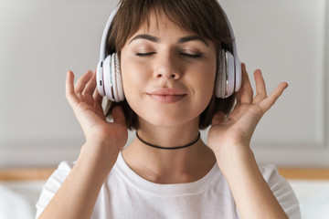Fototapeta premium Relaxing young beautiful woman indoors at home listening music with headphones.