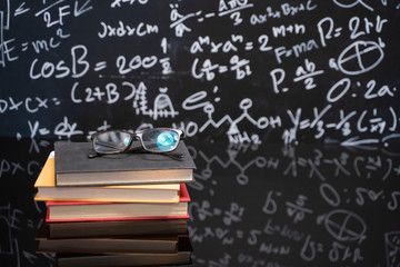 Glasses on the pile of old books on black table with a blackboard in the background.
