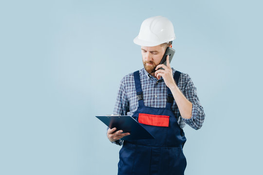 Conserned construction worker in a white helmet and blue overalls with a phone