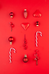 Merry Christmas composition with red baubles, holly berries, candy and cones on bright red...
