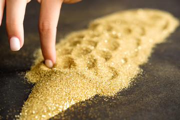 Woman draws on golden shining sand on black background.  Gold mining