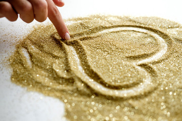 Woman draws heart shape on golden shining sand on white background. St. Valentine's Day, love card...