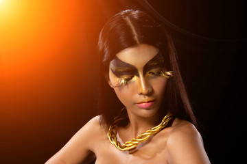 Fashion Young Asian Woman Tanned skin fancy eyelash black straight hair beautiful make up fashion decorate with Golden Foil or Gold leaf with bracelet and earrings. Studio Lighting dark Background