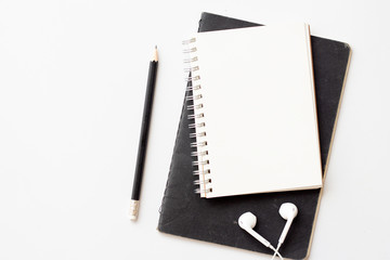 Notebook with black book, pencil and earphone on white office desk. minimal and modern work space. 