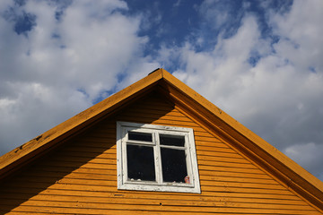 Part of typical house in Lithuania, Trakai. Antique old house. Triangular roof with yellow wooden walls and white windows and blue sky background.
