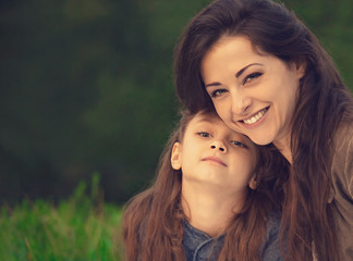 Beautiful young laughing mother embracing her cute long hair daughter on summer green grass background. Portrait of picnic relaxing time. Toned