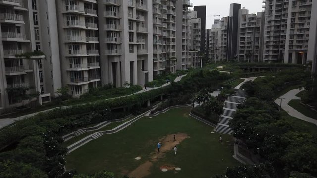 Handheld stabilized static view of kids playing cricket in a landscaped garden in-between a high-rise residential apartment complex in Gurugram, India- a financial and technology hub. 