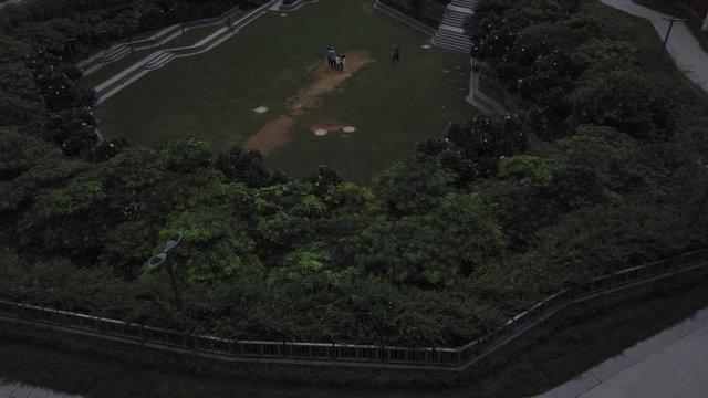 Slow tilt up view from a bunch of kids playing cricket in a landscaped garden in-between a high-rise residential apartment complex to a cloudy sky in Gurugram, India- a financial and technology hub. 