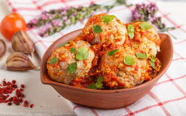 Pork meatballs with tomato sauce, oregano leaves, spices and herbs in clay bowl on a white wooden background with linen textile. side view