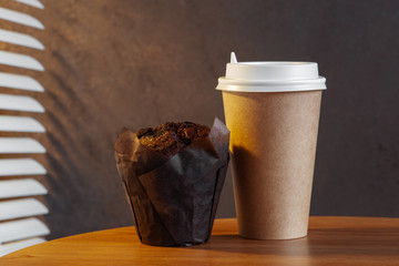 Paper cup of morning coffee and chocolate muffin on the table