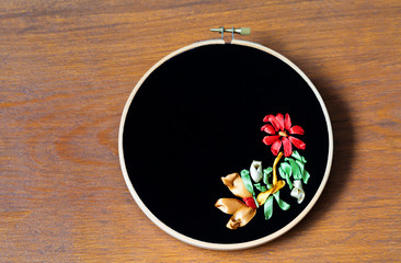 Hand embroidery with red, gold and green satin ribbons of flowers pattern on black velvet. Hobby, craft and needlework (embroidery was made by the author of the photo). Place for text, flat lay