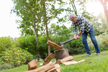 Senior man cutting logs, working in the garden