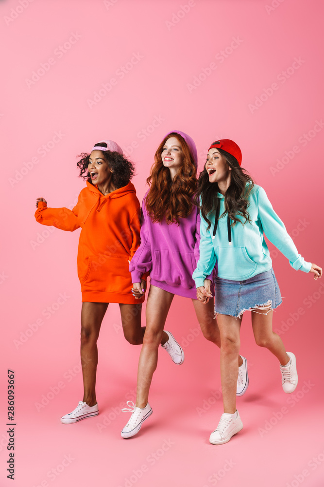 Wall mural Three happy young girls wearing colorful hoodies standing - Wall murals