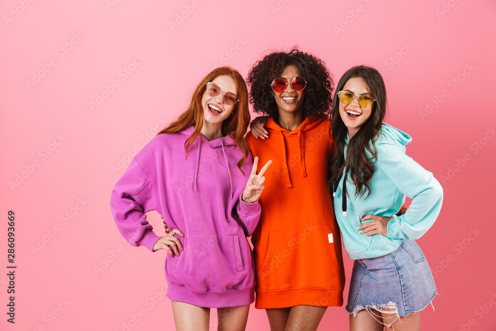Wall mural three happy young girls wearing colorful hoodies standing - Wall murals