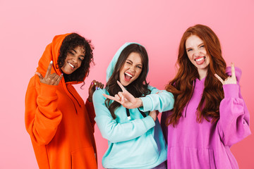 Amazing young three multiethnic girls friends posing isolated over pink wall background showing...