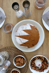 Homemade sponge cake served on a table with dishware, cookies, nuts and vase of flowers. Top view.