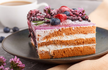 Berry cake with milk cream and blueberry jam on blue ceramic plate with cup of coffee and fresh blueberries on a gray concrete background with orange textile. side view, selective focus