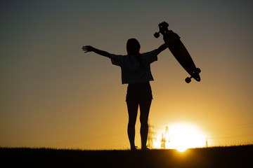 girl looks at sunset holding a longboard in her hand