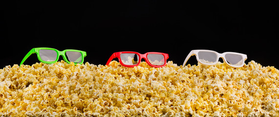 Cinema glasses installed on scattered popcorn isolated on black background