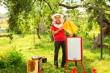 A beekeeper in a protective cap launches into work a honey extractor on the bee farm. Beekeeping
