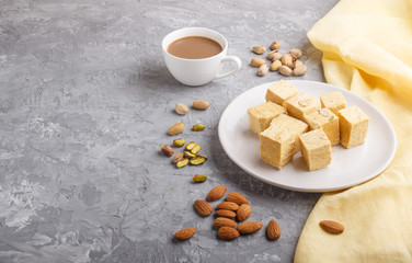 traditional indian candy soan papdi in white plate with almond and pistache on a gray concrete background. side view