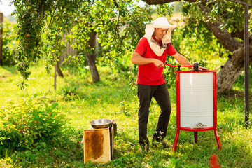 A beekeeper in a protective cap launches into work a honey extractor on the bee farm. Beekeeping
