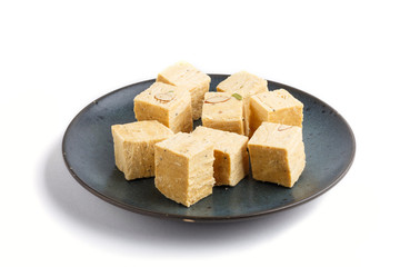 traditional indian candy soan papdi in blue ceramic plate isolated on a white background. side view