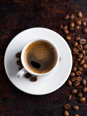 White espresso coffee Cup on vintage rusty background with scattered roasted coffee beans