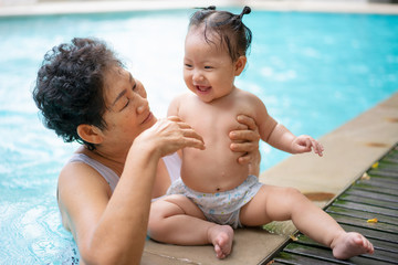 Senior asian woman is enjoying time with her adorable one year old grandchild in a swimming pool.