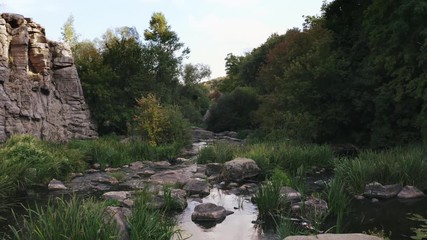 Aerial shot with drone flying close to the water above rhe rocks in canyon during sunny day