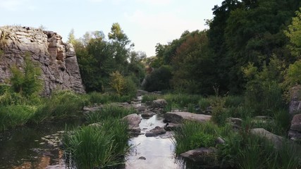 Aerial shot with drone flying close to the water above rhe rocks in canyon during sunny day