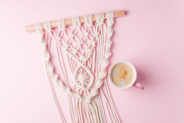 Creative flat lay concept, coffee cup and macrame panel on pastel pink background and copy space, minimal style, saint valentine romance trendy composition