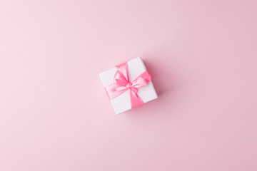 Present or gift box with pink satin bow on pink paper background, top view. Valentines day greeting card, black friday sale, congratulations concept. Flat lay style