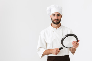 Image of handsome chief man in cook uniform looking at camera and holding frying pan