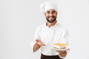 Image of professional chief man in cook uniform smiling and holding plate with piece of cheesecake