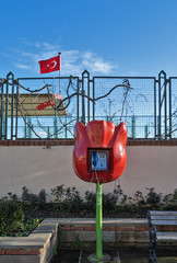 Tulip shaped public phone in front of grunge wall with metal fence and on background of flag of Turkey and blue sky . Sultanshmet district, Istanbul. 