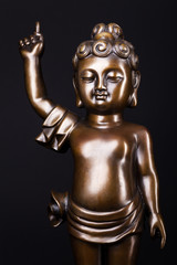 Young prince Siddhartha Gautama vith rized finger. The figure made of metal isolated on a black background.