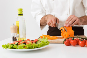 Cropped image of young cook man in uniform cutting vegetable salad on wooden board