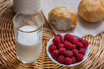 ripe red raspberries, a glass of milk and fresh homemade buns on a wicker wooden background