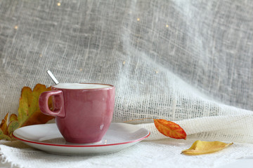 red cup with a foamy cappuccino and the last fallen leaves on the table. autumn coffee