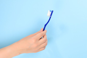 Woman holds toothbrush with toothpaste in her hand on a blue background.