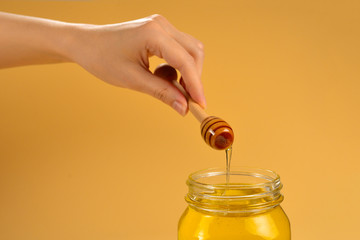 Dipper with honey in woman hand on orange background. Space for text or design.