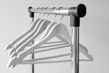 Empty clothes hangers on metal rail against grey background. Rectangular metal clothing rail with empty white wooden coat hangers.