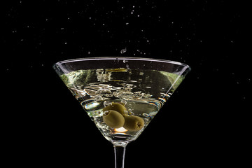 a glass of martini and a splash from falling olives