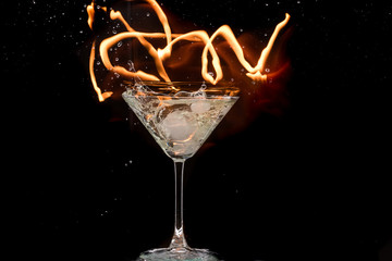 glass of martini with olives and ice on a black background and fire